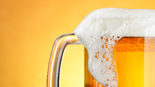Bicchiere di birra con schiuma che scivola via su sfondo giallo